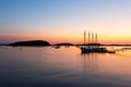 Four-mast sailboat and other smaller boats anchored in Frenchman Bay during a pink and orange sunrise, with the Porcupine islands