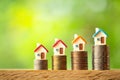 Four miniature house models on coin stacks on greenery blurred background