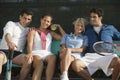 Four mixed doubles tennis players sitting on bench at tennis court portrait