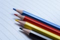 Four multi-colored pencils - blue, red, yellow, black. lie on an open notebook Royalty Free Stock Photo