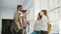 Four multi-ethnic studens are standing in big white spacious hall in college talking to each other in positive way. They