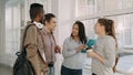 Four multi-ethnic studens are standing in big white spacious hall in college talking to each other in positive way. They