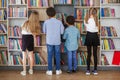 Four multietnic children look for books near bookshelves and read together in school library. Back