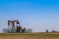 Four oil well pump jacks on prairie one close-up and three in the distance pumping oil near horizon under clear blue sky Royalty Free Stock Photo
