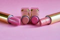 Four old used lipstick tubes lie on a pink background