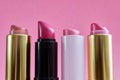 Four old used lipstick tubes stand on a pink background