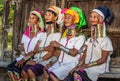 Four Padaung women in traditional dress and with metal rings around their neck are sitting next to each other in the village