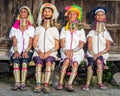 Four Padaung women in traditional dress and with metal rings around their neck are sitting next to each other in the village