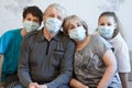 Four people portrait, grandparents with their teen age grandchildren wearing facial masks, sitting on sofa in a domestic room Royalty Free Stock Photo