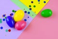 Four plastic easter eggs in blue, green, yellow and pink, with confetti on a geometric mutli-colored background