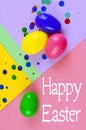 Four plastic easter eggs in blue, green, yellow and pink, with confetti on a geometric mutli-colored background