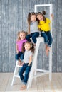 Four pretty cheerful girls triple twins sisters in jeans are sitting on a stepladder in front of a wooden wall background in
