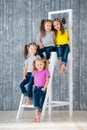 Four pretty cheerful girls triple twins sisters in jeans are sitting on a stepladder in front of a wooden wall background in