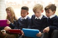 Four primary school children sitting on the floor in front of a window using tablet computers during break time, close up