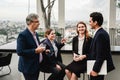 Four professionals network on a rooftop terrace, sharing drinks and conversation with a city skyline in the background Royalty Free Stock Photo