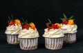 Four puff pastries with cream, chocolate cakes with biscuits. Close-up on a black background. In a white paper cup.