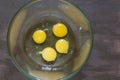 Four raw chicken yolks and whites in glass bowl on wooden table Royalty Free Stock Photo