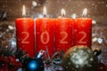 Four red Advent candles with 2022 figures on them and Christmas decorations lying in the snow as a template