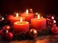 Four red Advent candles within lush evergreen branches. Christmas time, Advent season. Flickering flames cast soft, inviting glow