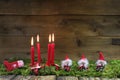 Four red burning christmas candles on wooden background with green moss.