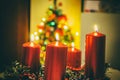 Four red candles burning on advent wreath with blurred colorful christmas tree with glowing lights in the background on evening Royalty Free Stock Photo