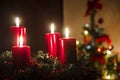 Four red candles burning on advent wreath with blurred colorful christmas tree with glowing lights in the background on evening Royalty Free Stock Photo