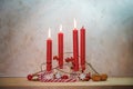 Four red candles, three are lit for the third Sunday before Christmas, Advent decoration on a wooden table against a rustic wall,