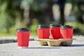 Four red paper coffee cups with black lids on a stand stand on a concrete surface on a blurred background of city Royalty Free Stock Photo