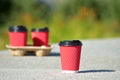 Four red paper coffee cups on a stand stand on concrete on blurred background of greens, one of them stands separately Royalty Free Stock Photo