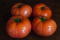 Four red tomatoes on a wooden surface