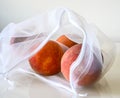 Four ripe peaches in a white eco friendly bag on a white table Royalty Free Stock Photo