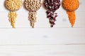 Four round containers with legume crops peas, nut, beans, red lentils on a white wooden background.