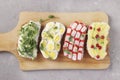 Four sandwiches on toast with peas microgreens, pineapples, red currant, crab sticks and quail eggs on wooden board on gray