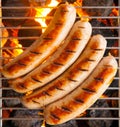 Four sausages called bratwurst, grilling over hot coals on a BBQ