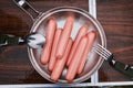 Four sausages frankfurter wurst boiling in hot water in pan.