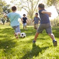 Four schoolboys playing football in the park, square format