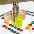 Four sets of watercolor paints, many brushes in a plastic jar and glasses