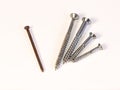 Four shiny screws and one rusty nail lying on white background