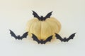 Four silhouettes of flying black paper bats next to a yellow pumpkin on a light background.