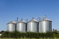 Four silver silos in field under blue sky