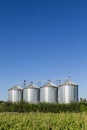 Four silver silos in field under blue sky