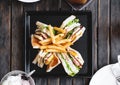 Four slices sandwiches with french fried, on black square dish, on wooden table