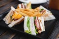 Four slices sandwiches with french fried, on black square dish, on wooden table Royalty Free Stock Photo