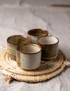 Four Small Ceramic Cups Arranged on Woven Mat with Rustic Texture and Earthy Tones Royalty Free Stock Photo