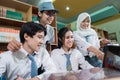 four smiling high school students looking at a laptop screen while using a laptop to study together at a desk Royalty Free Stock Photo