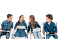 Four smiling kids in denim clothes sitting on chairs and using digital tablets isolated on white. Royalty Free Stock Photo