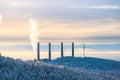 Four smoke stacks and a wind power plant by a forest at winter.. Royalty Free Stock Photo