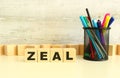 Four stacked wooden cubes with the letters ZEAL on a white desktop on a gray background.