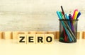 Four stacked wooden cubes with the letters ZERO on a white desktop on a gray background.