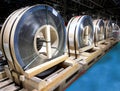 Four stainless steel coils laid on edge, packed on wooden pallets on the blue floor of a factory, cold metal stamping, sheet metal